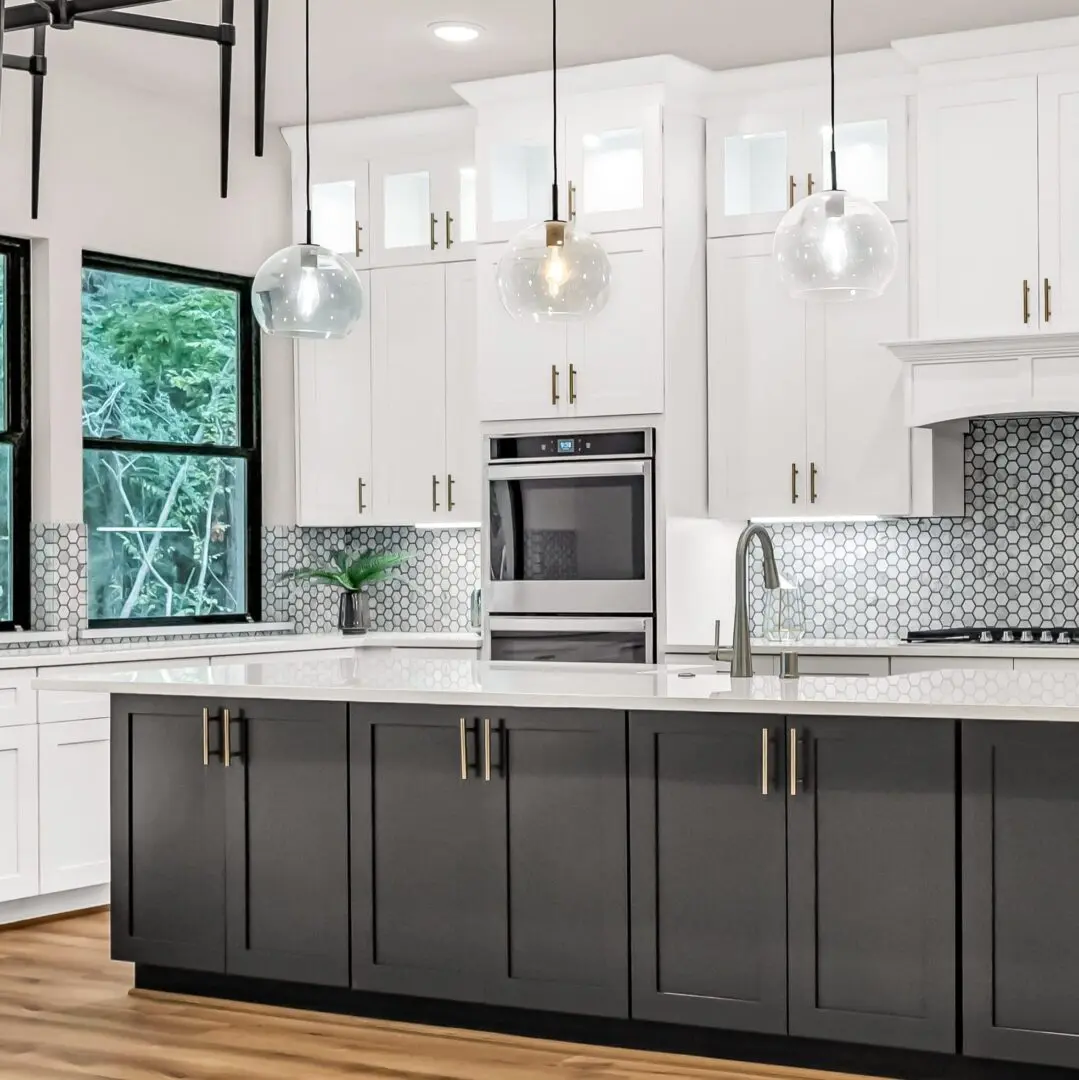 Modern kitchen featuring white cabinetry, a dark island, hexagonal backsplash, pendant lighting, and large windows with greenery outside.