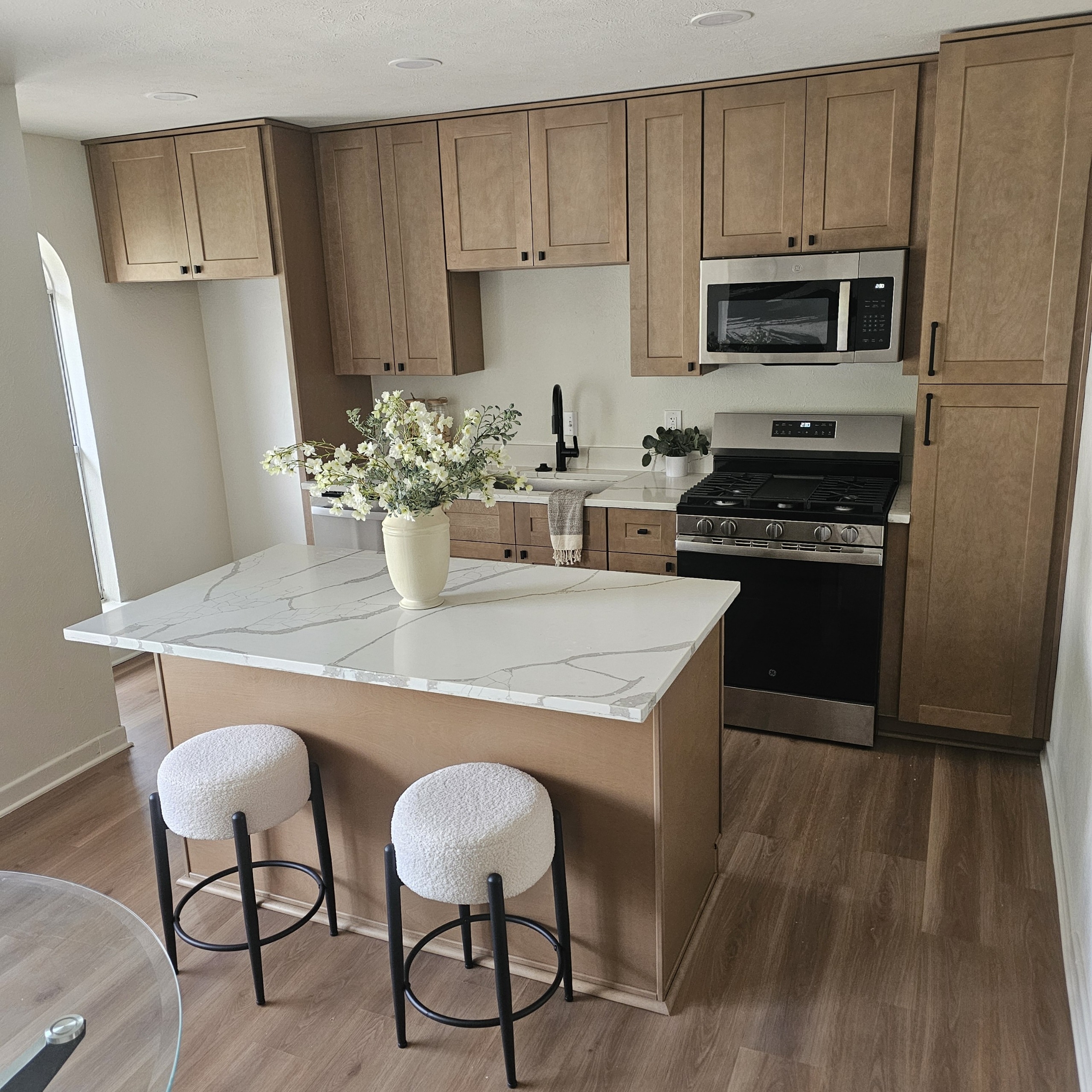 Modern kitchen featuring wooden cabinets, marble island top, and stainless steel appliances. A vase of flowers enhances the inviting atmosphere.