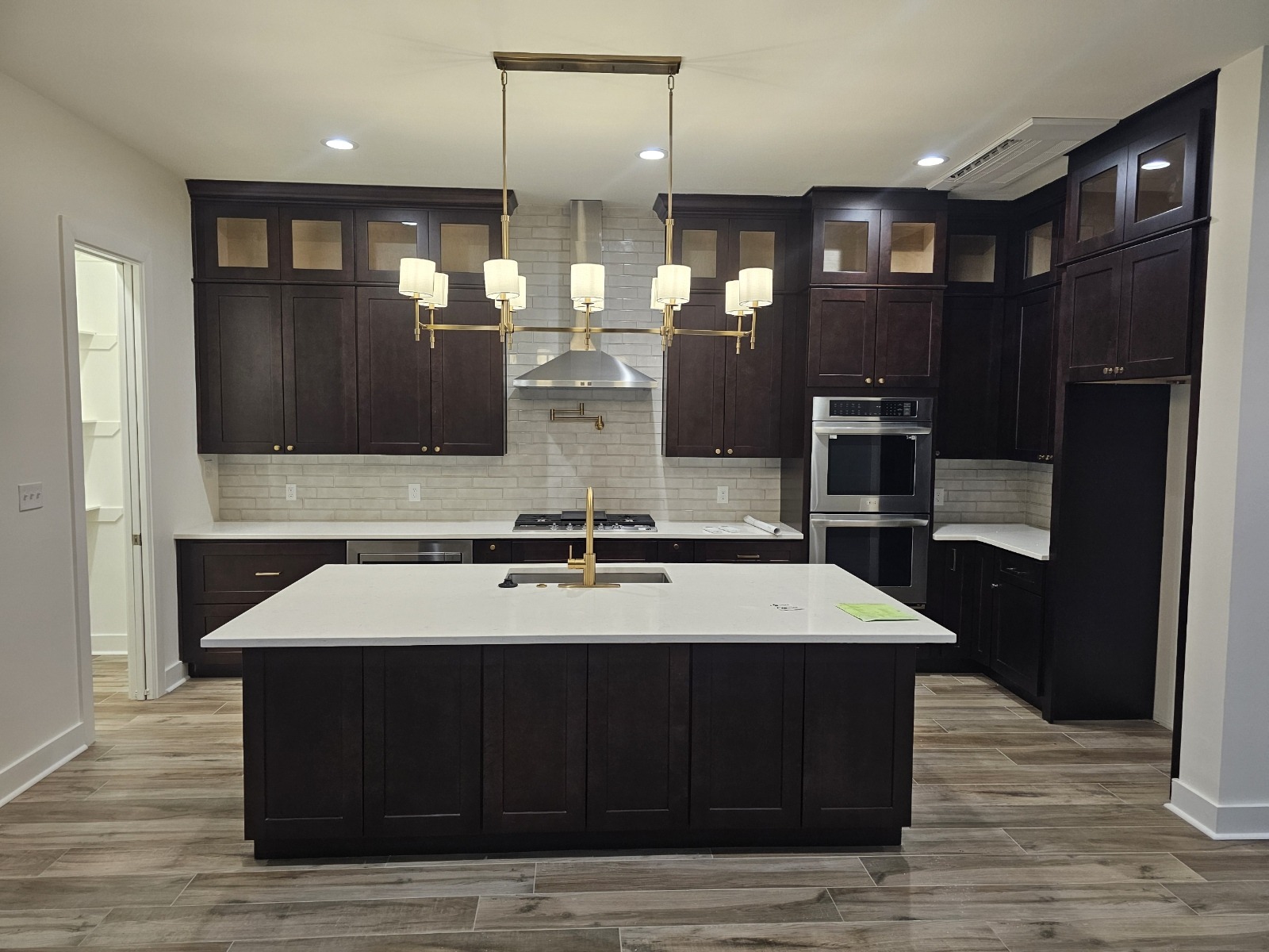 Modern kitchen featuring dark wood cabinets, a central island with a sink, stainless steel appliances, and stylish pendant lighting.