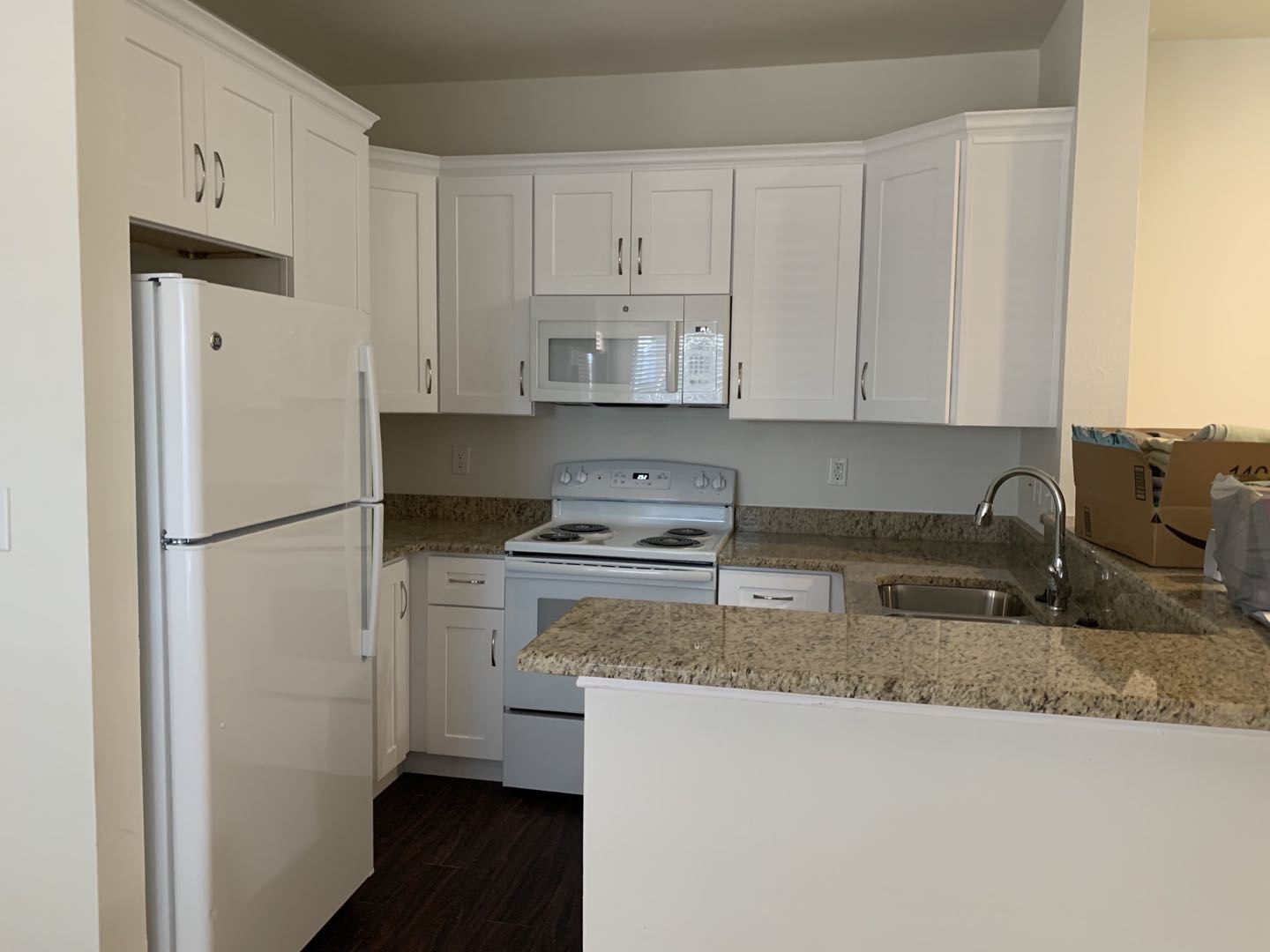 Newly renovated kitchen featuring white cabinets, granite countertops, and modern appliances including a refrigerator, stove, and microwave.