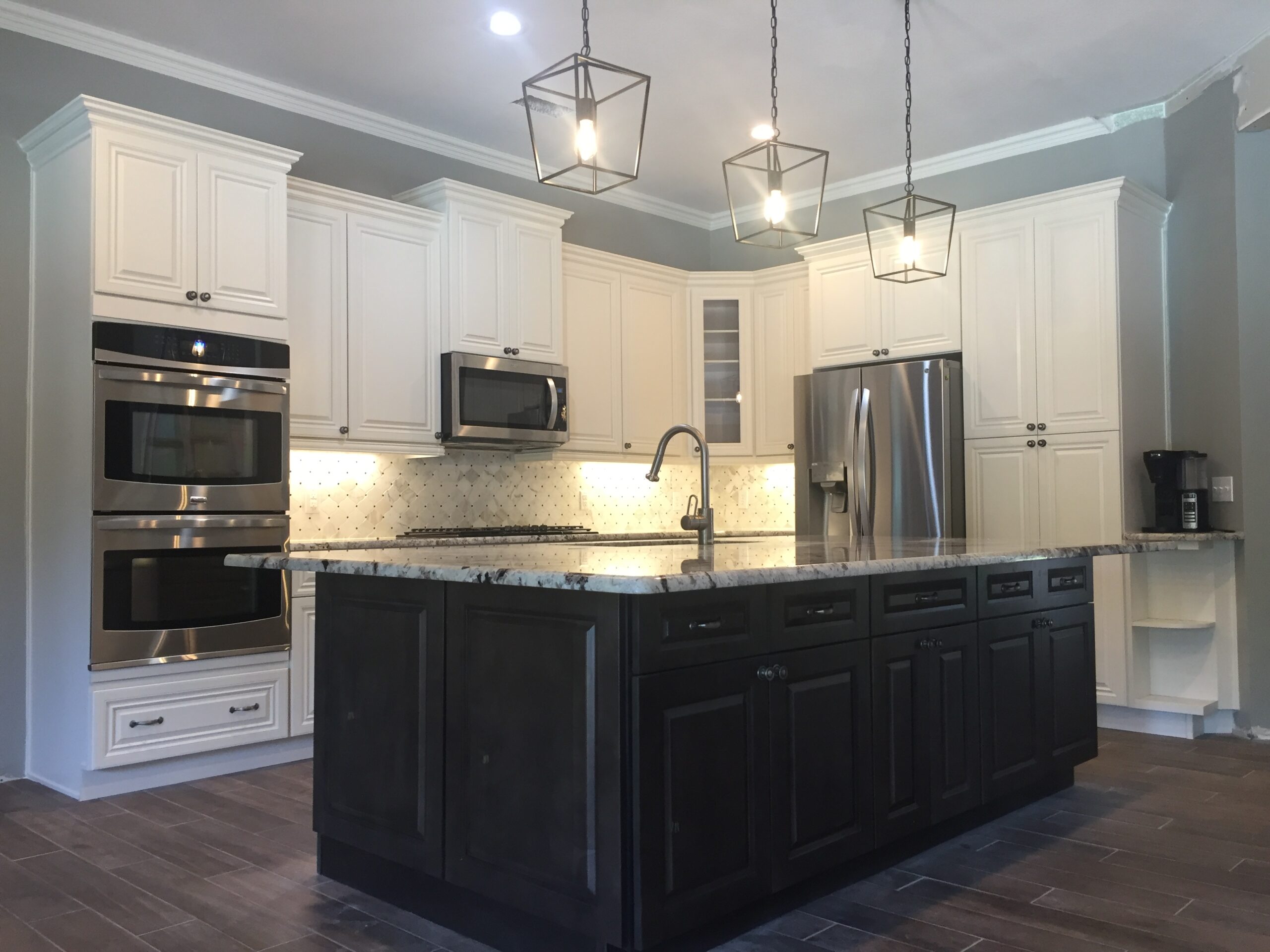 Modern kitchen featuring a central island, stainless steel appliances, and white cabinetry. Pendant lights illuminate the space, highlighting its contemporary design.