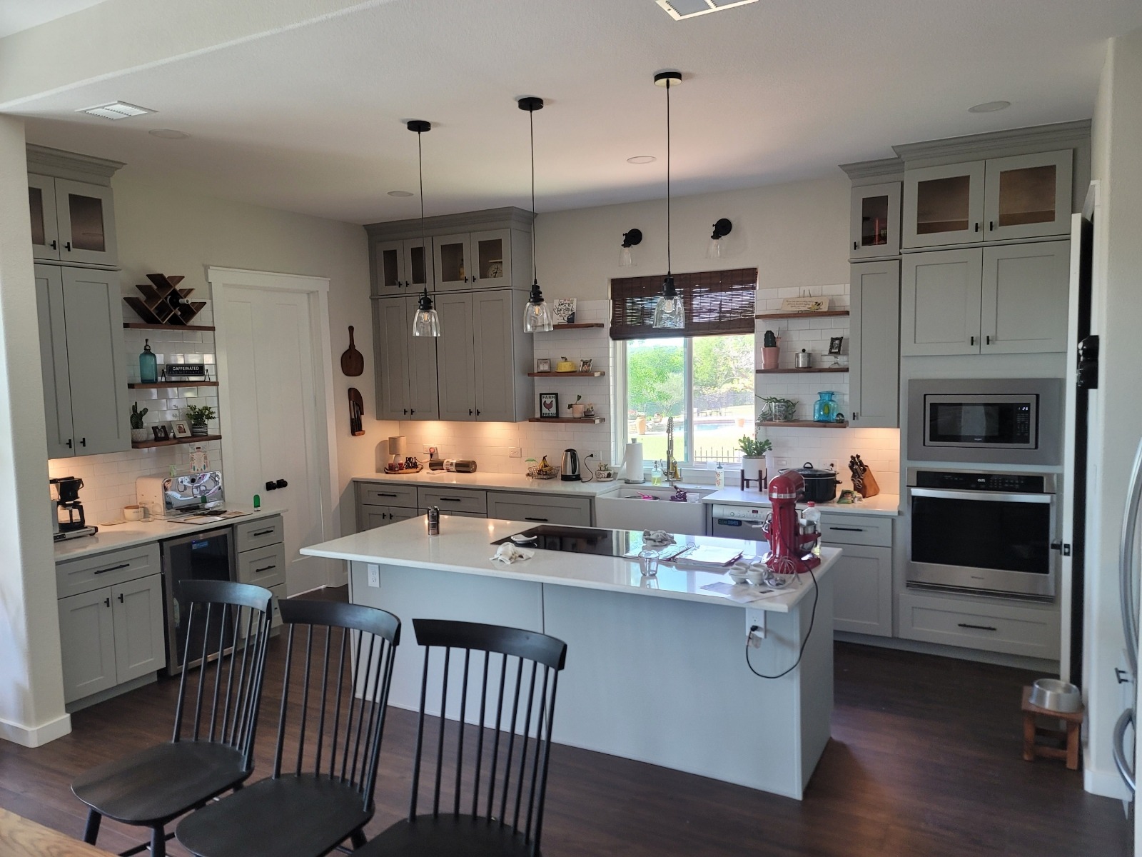 Modern kitchen featuring gray cabinetry, white countertops, and black accent chairs. Natural light floods in through a large window, enhancing the inviting atmosphere.