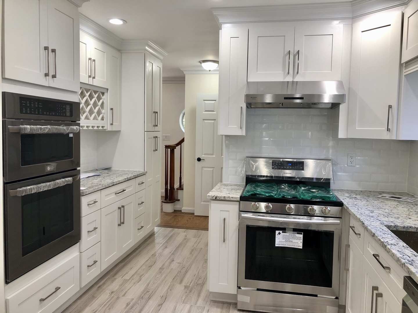 Modern kitchen featuring white cabinetry, stainless steel appliances, and a grey granite countertop. Shiny tiles and a door leading to another area enhance the design.
