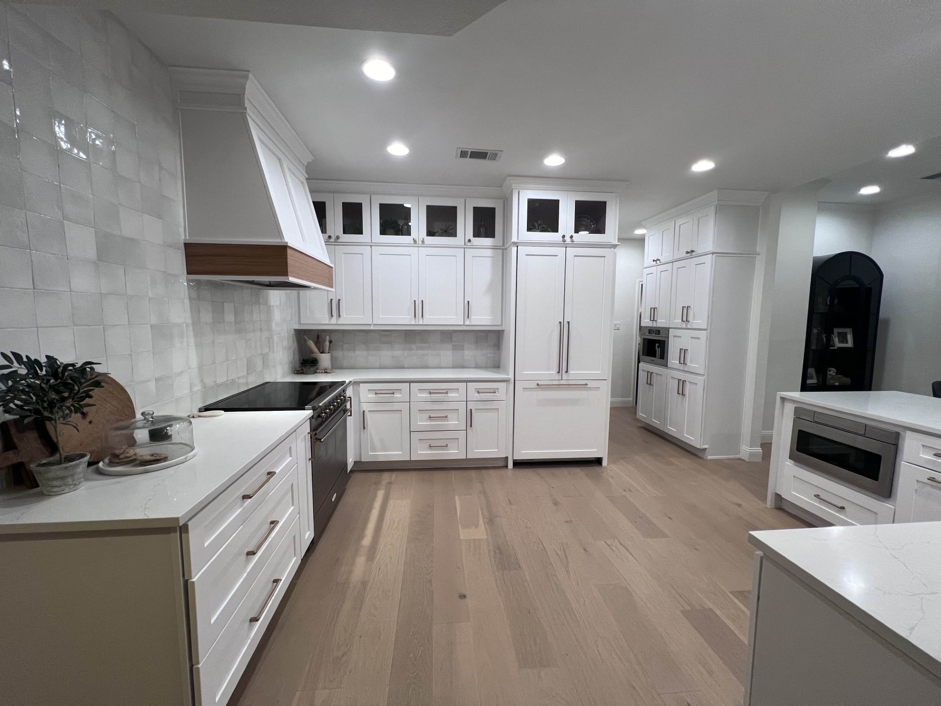 Modern kitchen featuring white cabinetry, stainless steel appliances, and wooden accents. Bright lighting highlights the spacious layout and stylish design.
