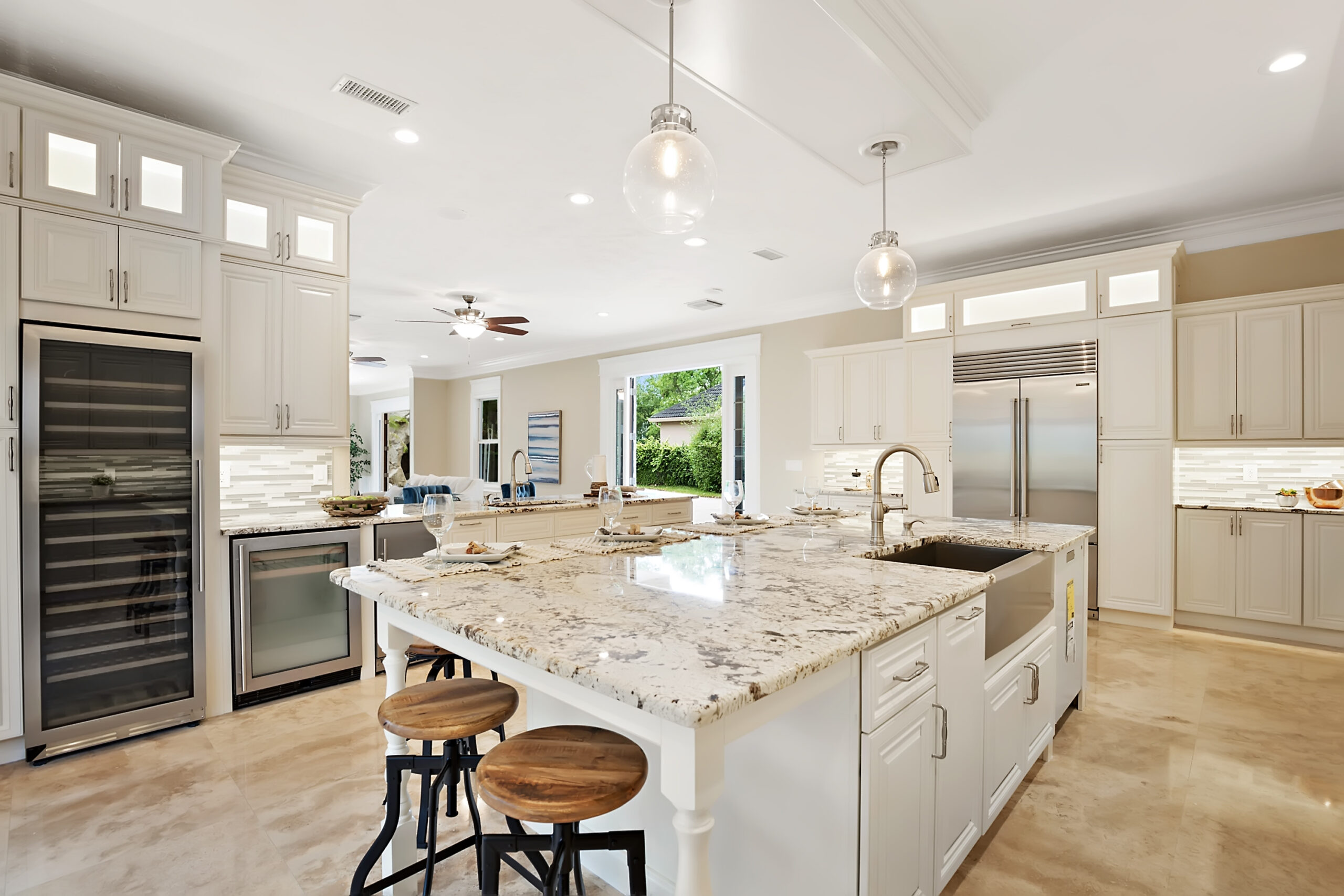 Modern kitchen featuring white cabinetry, a large granite island with seating, stainless steel appliances, and natural light from windows.