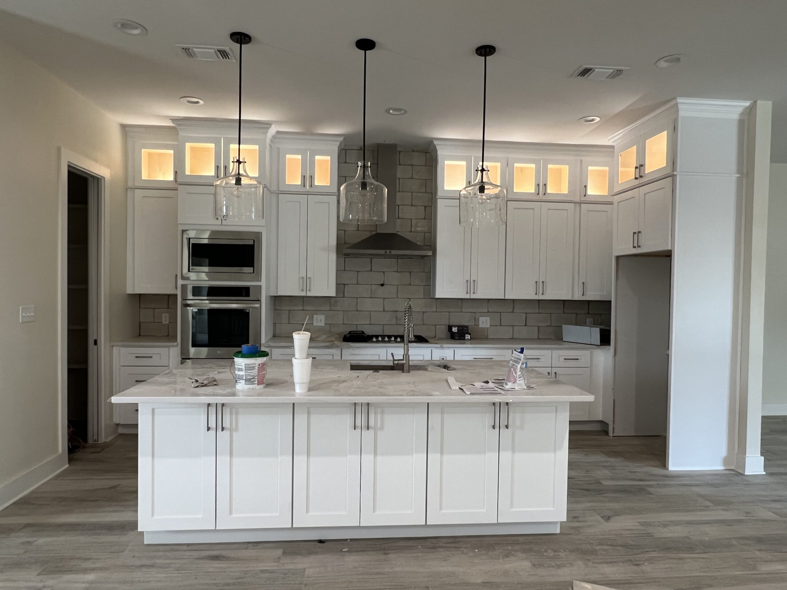 Modern kitchen featuring white cabinetry, marble countertop, and pendant lighting. The open design includes built-in appliances and illuminated shelf spaces.